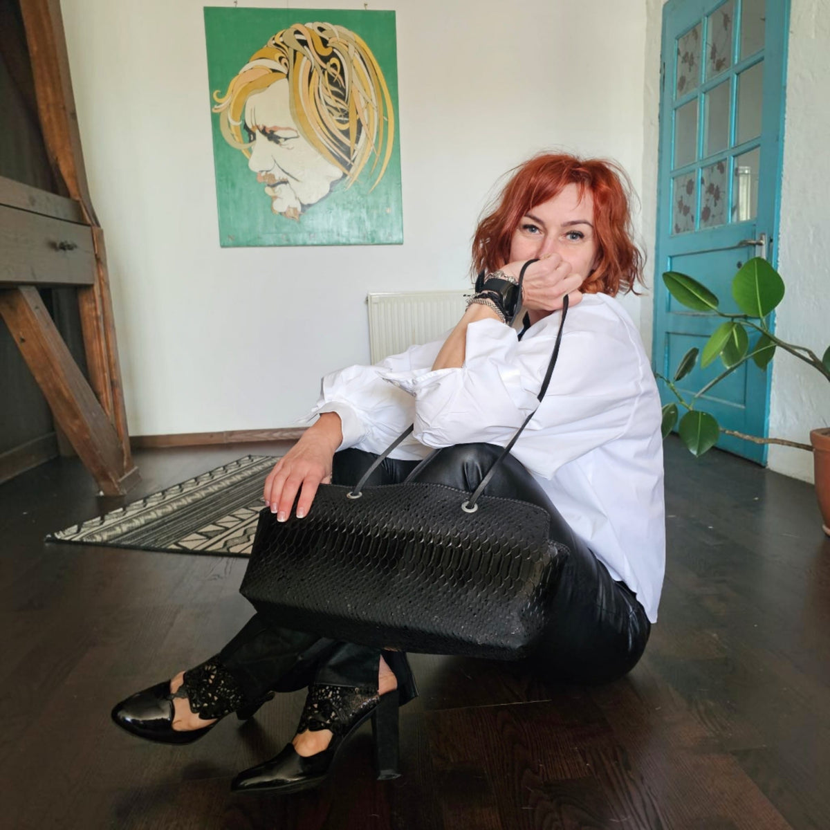 Alexandra seated on a wooden floor with the handmade black snake-embossed leather shoulder bag - AG Design, Arad, Romania