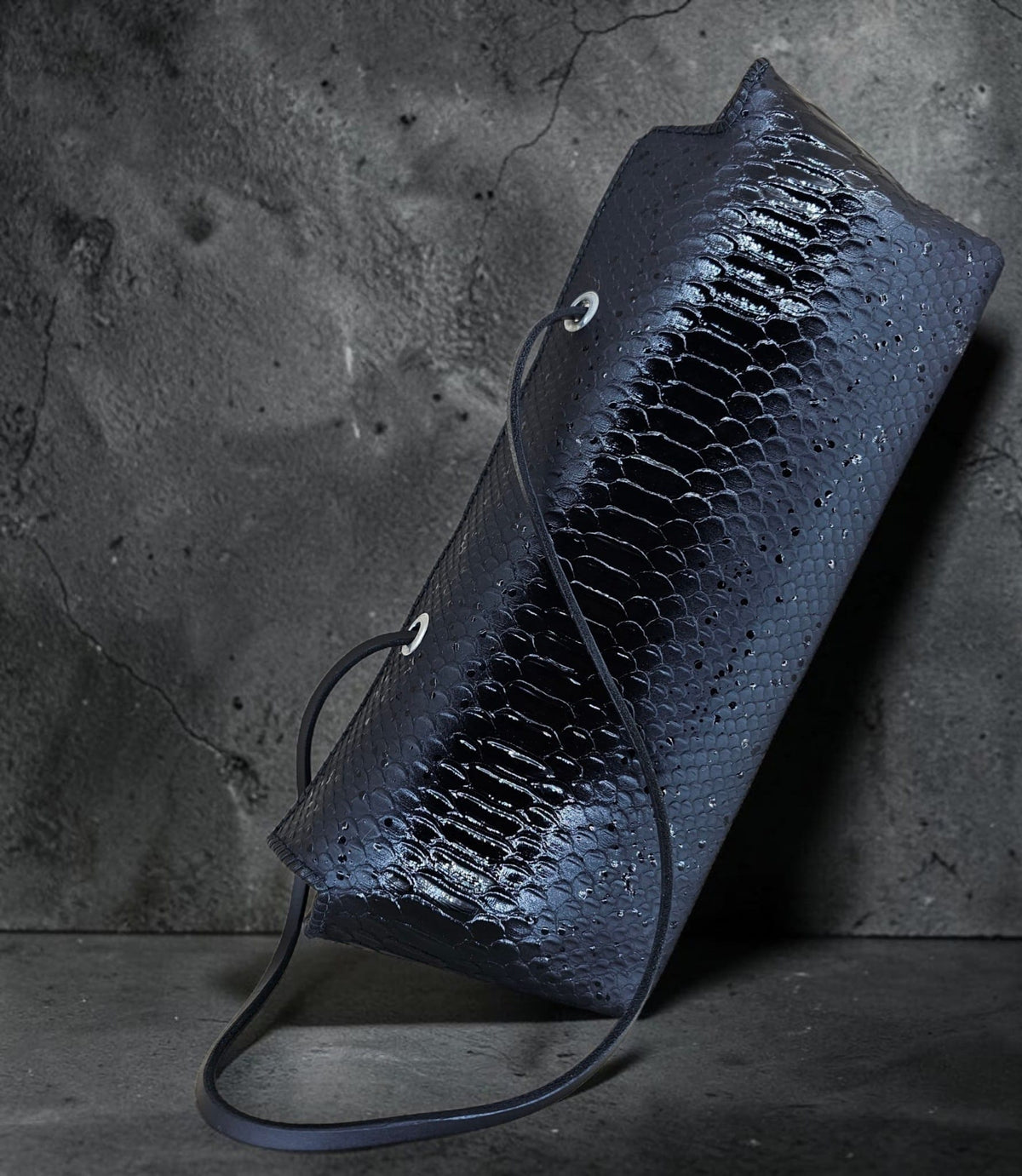 Black snake-embossed leather shoulder bag with slender fixed leather straps through metal eyelets, on a black background - AG Design, Arad, Romania
