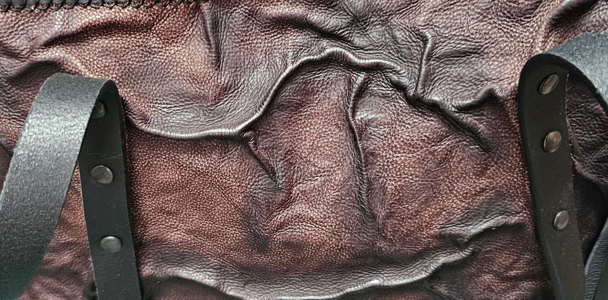 Close-up of the hand-worked relief on a brown and black leather shoulder bag, ridges and grain catching the light - AG Design, Arad, Romania