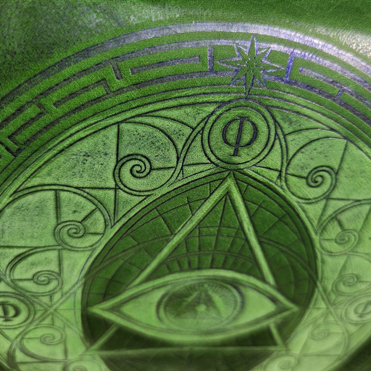 Detail of the eight-pointed star, Phi symbol and spirals embossed in blue on a green leather crossbody bag - AG Design, Arad, Romania